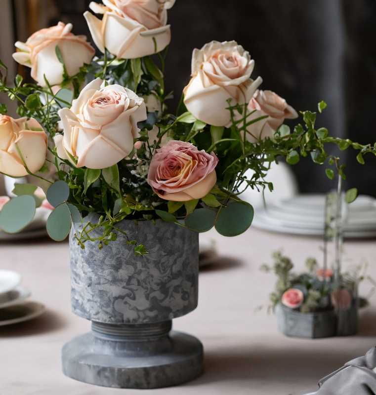 A tablescape featuring a delicate arrangement of roses in elegant grayish stone vases.