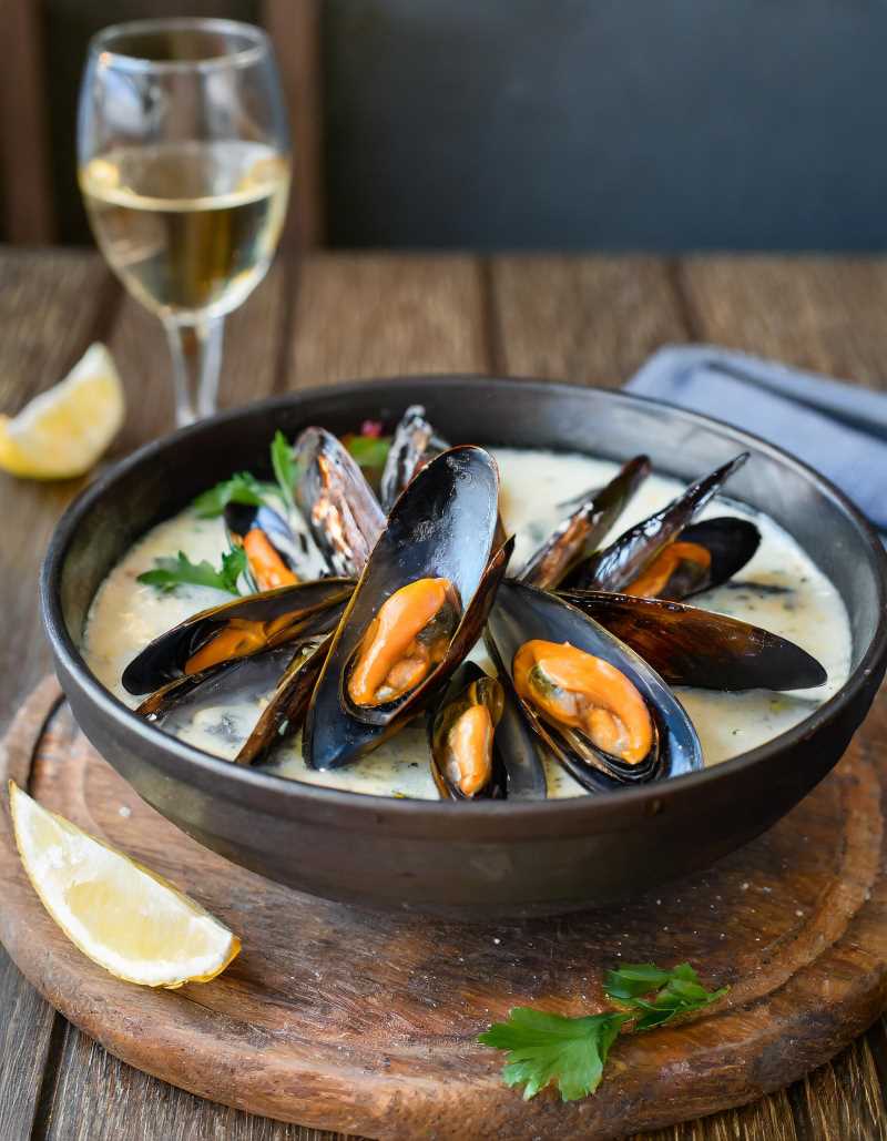 A bowl of cooked mussels in a white wine broth, sprinkled with fresh herbs.