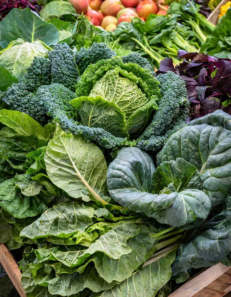 A diverse selection of leafy greens at a market, including kale, collard greens, bok choy, and spinach.