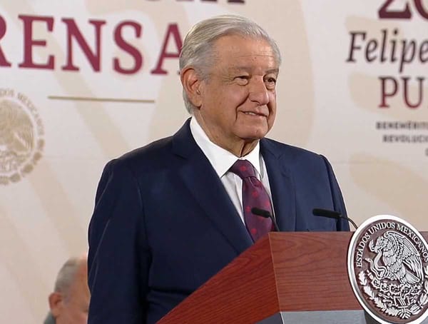 A photo of AMLO standing at the podium during the morning conference, with a graph projected behind him.