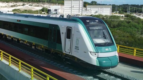 A sleek, modern train with the Maya Train logo pulls into a brightly lit Playa del Carmen station.