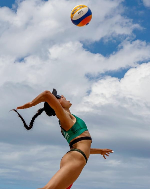 A beach volleyball player in mid-air dive reaching for the ball, surrounded by Mexican fans in Guadalajara.