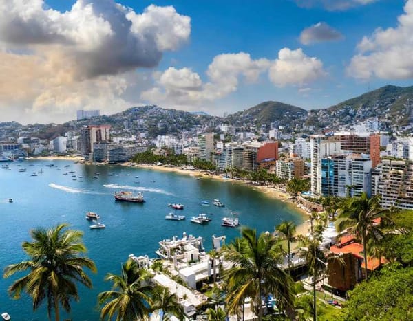 A panoramic view of Acapulco's skyline with colorful buildings and palm trees lining the coast.