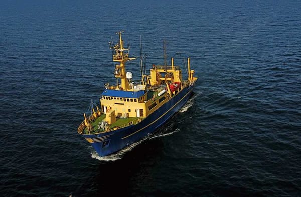A research vessel “El Puma” with scientific equipment visible on the deck, sailing on blue ocean waters.