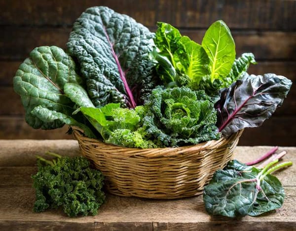 A basket overflowing with leafy greens, including kale, collard greens, spinach, and Swiss chard.