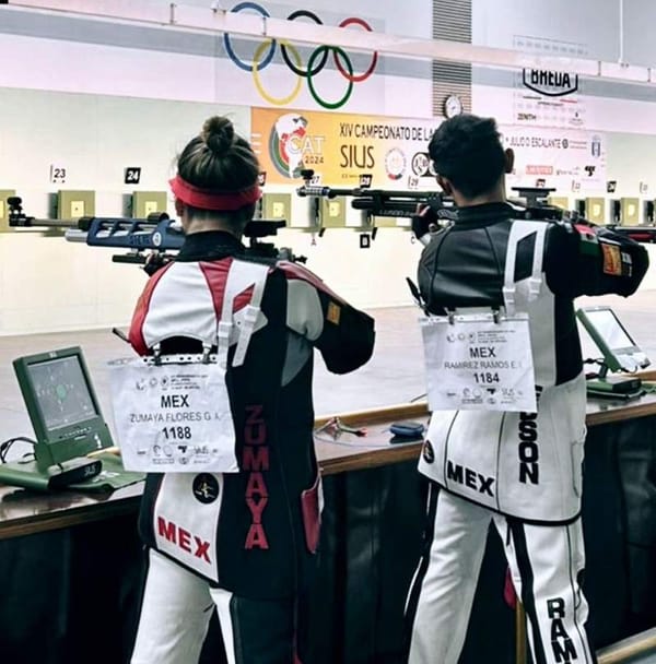 Mexican athletes wearing shooting gear and concentrating on aiming rifles at a shooting range.