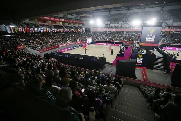 Indoor stadium with spectators cheering enthusiastically during a beach volleyball match.