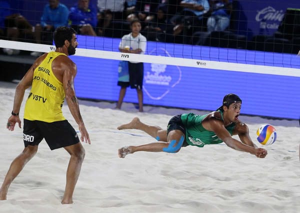 Two male beach volleyball players in action, spiking the ball. Fans in the background.