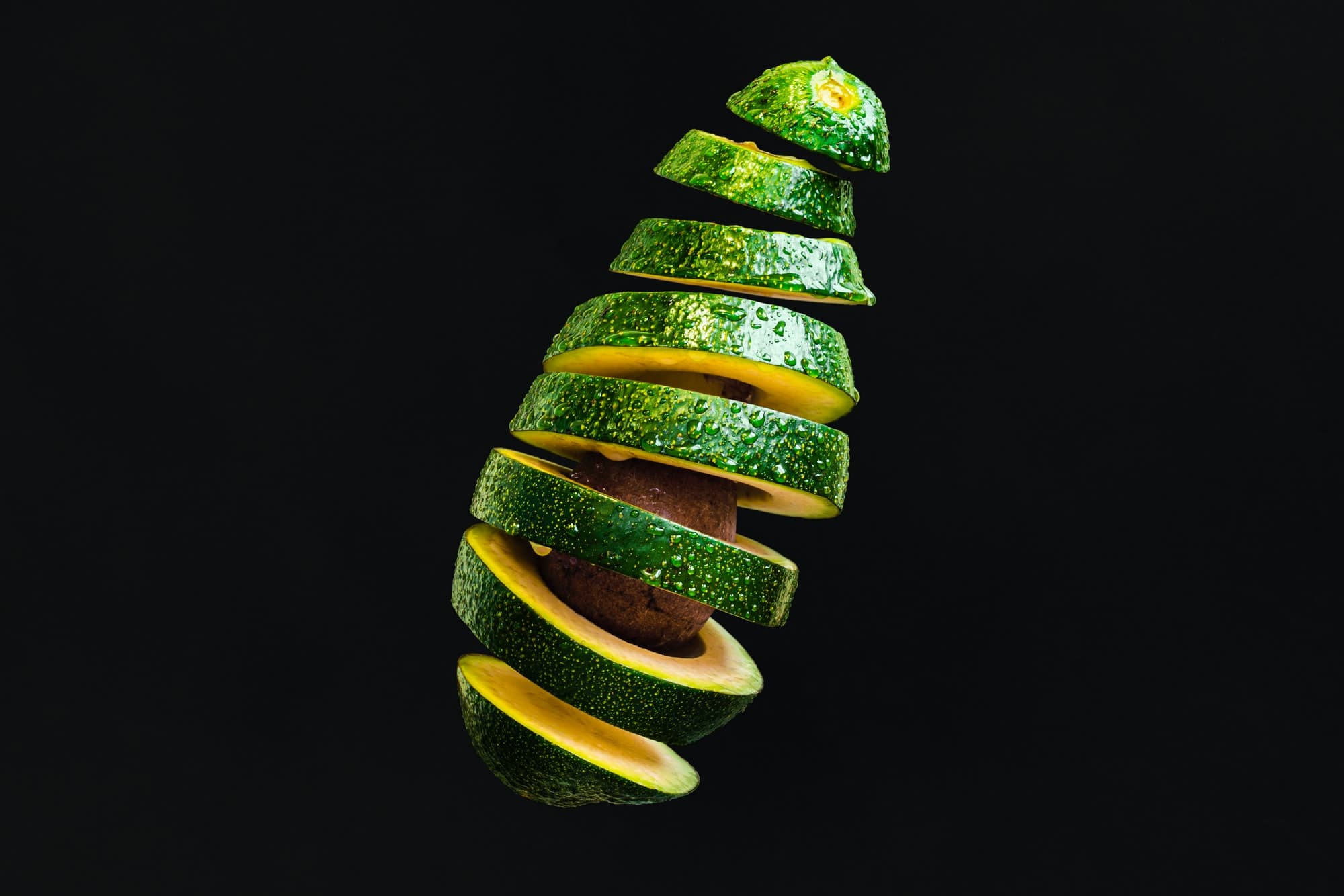 Avocado fruit cut into slices on top of black background.