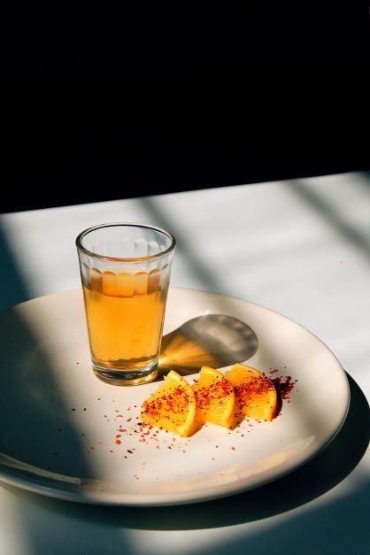 A glass of young or gold tequila on a plate with three slices of orange.
