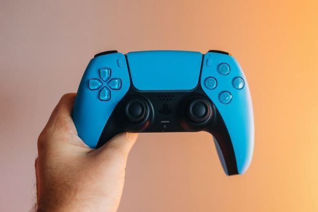 A hand holding a blue PlayStation 5 joystick into the air.