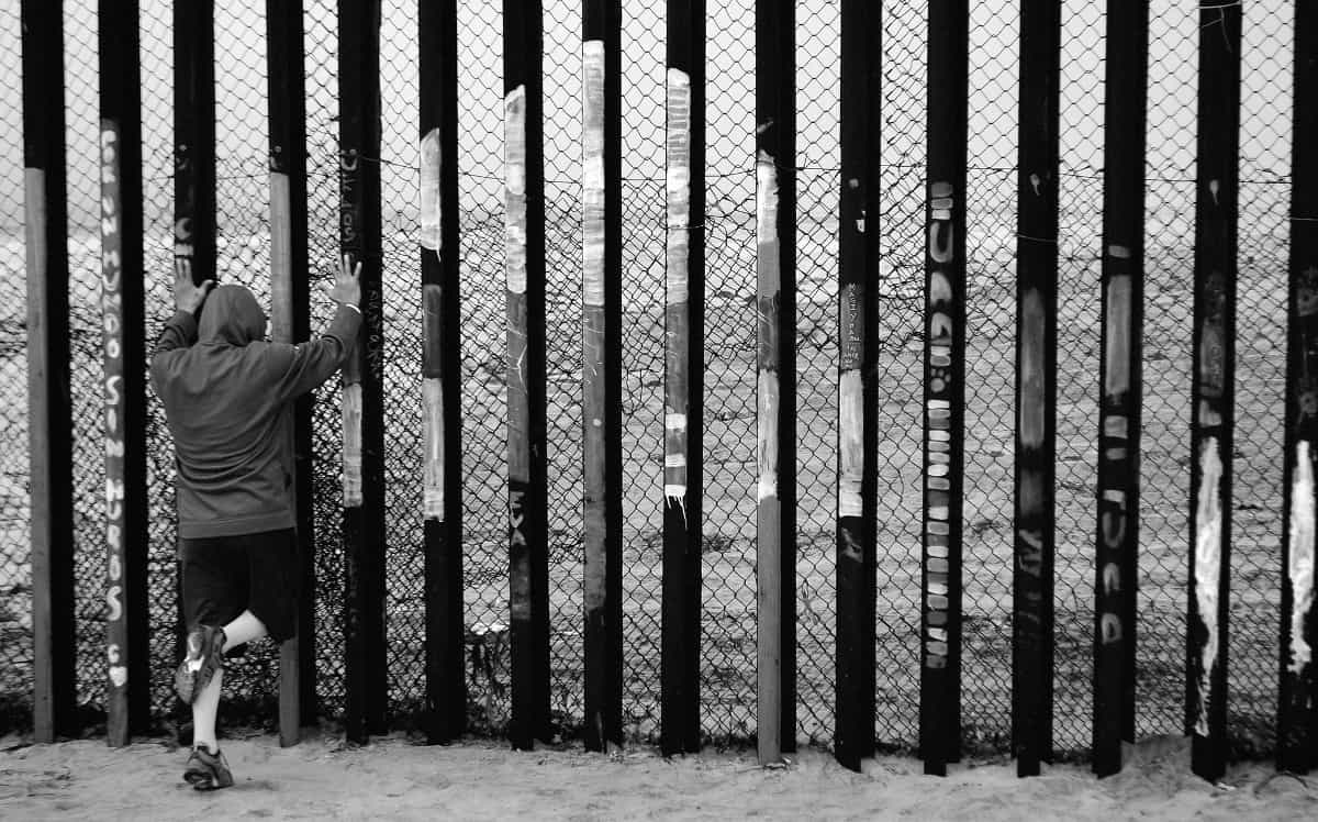 A person can be seen leaning against the U.S. - Mexico border wall or fence in the north of the country.