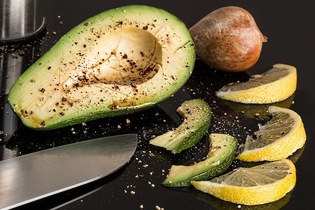 Fresh avocado and lemon slices cut by a knife on the table.